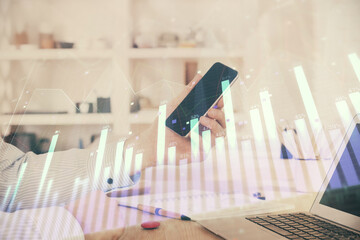 Double exposure of man's hands holding and using a digital device and forex graph drawing. Financial market concept.