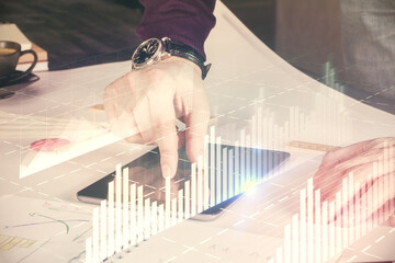 Double exposure of man's hands holding and using a digital device and forex graph drawing. Financial market concept.