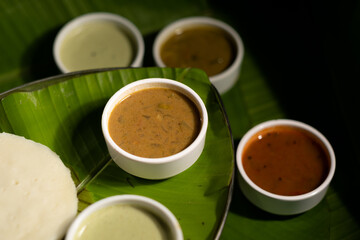 A a staple of breakfast in southern India, a savory rice cake ('idli') is served alongside various sauces against a backdrop of banana leaves.