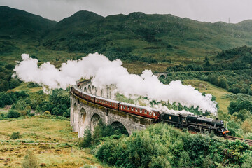 A steam train crossing the Glenfinnan viaduct in the Scottish Highlands made famous by the Harry Potter movies. The Jacobite steam train crossing the bridge with steam in Scotland United Kingdom - obrazy, fototapety, plakaty