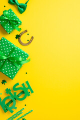St Patrick's Day concept. Top view vertical photo of green gift boxes with bows horseshoe irish party glasses bow-tie straws and shamrock shaped confetti on isolated yellow background with copyspace