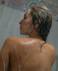 artistic photo of sensual woman in a soapy bath with foam behind the glass door taking a bath in the shower