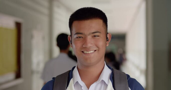Slow motion scene of a happy smiling male high school student standing on a corridor in a school building with a laptop backpack.