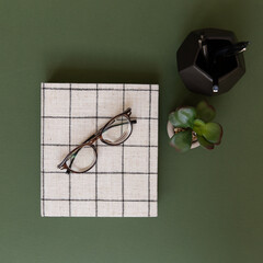 Trendy fabric planner scheduler with green background and black pen holder with glasses and plant.