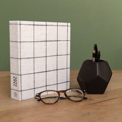 Trendy fabric planner scheduler with green background and black pen holder with glasses and plant.