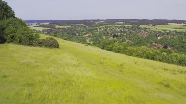 Drone shot of woman sitting with pet black Labrador dog on Streatley Hill in West Berkshire UK through summer field with village in background