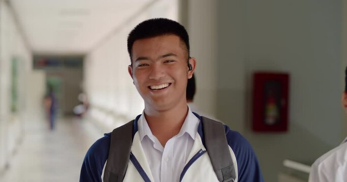 Slow motion scene of a happy smiling male high school student standing on a corridor in a school building with a laptop backpack.