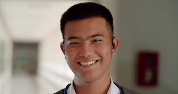 Slow motion scene of a happy smiling male high school student standing on a corridor in a school building with a laptop backpack.