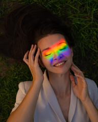 Top view of caucasian woman with rainbow ray on her face lies on green grass. 