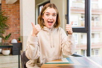 Fototapeta premium pretty caucasian woman smiling joyfully and looking happy, feeling carefree and positive with both thumbs up. home interior concept