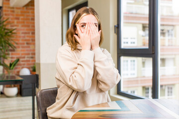 pretty caucasian woman covering face with hands, peeking between fingers with surprised expression and looking to the side. home interior concept