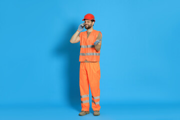 Man in reflective uniform talking on smartphone against light blue background