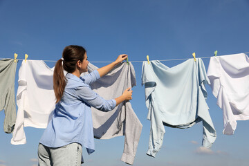 Woman hanging clothes with clothespins on washing line for drying against blue sky