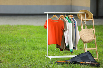 Clothing rack with different garments in yard, space for text. Garage sale