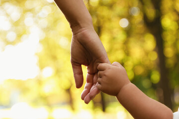 Daughter holding mother's hand outdoors, closeup. Happy family - Powered by Adobe