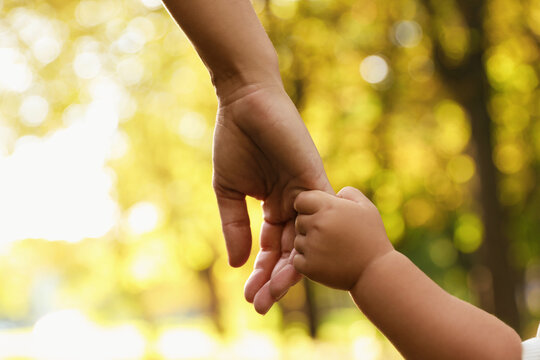 Daughter holding mother's hand outdoors, closeup. Happy family