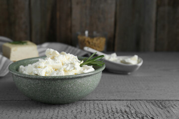 Delicious tofu cream cheese with rosemary in bowl on grey wooden table, space for text