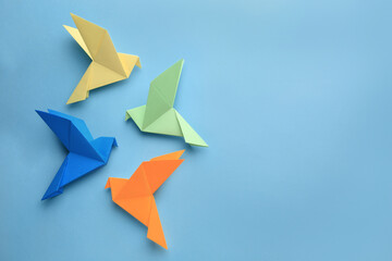 Fototapeta na wymiar Origami art. Colorful handmade paper birds on light blue background, flat lay. Space for text