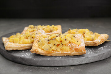 Fresh tasty puff pastry with sugar powder and kiwi on grey table, closeup