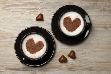 Cups of aromatic coffee with heart shaped decoration and chocolate candies on wooden table, flat lay