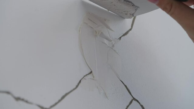 Worker's Hand Uses Putty Knife In Filling Cracks On The Wall With Concrete Caulk. closeup