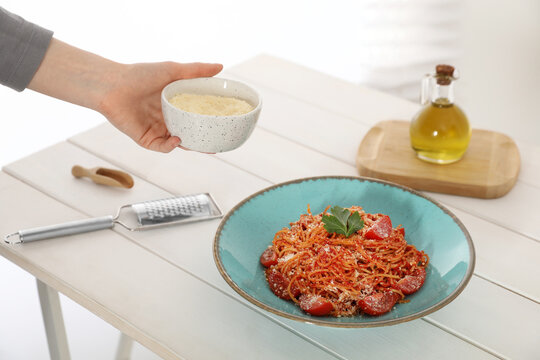 Food stylist holding grated cheese for spaghetti at white wooden table in studio, closeup
