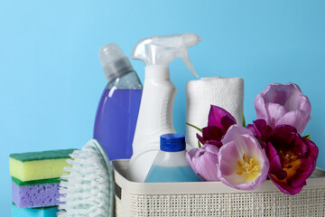 Spring cleaning. Basket with detergents, flowers and tools on light blue background, closeup