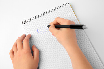 Child erasing doodle drawn with erasable pen in notepad against white background, top view