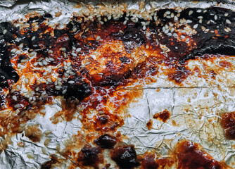 Greasy stains on a baking sheet with foil close-up. Challenges of completing oven chicken cooking.