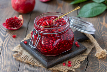 Glass jar of homemade canned pomegranate tea made from fresh pomegranate juice and seeds with spoon full of seeds on top. Dark wooden table, selective focus, horizontal.