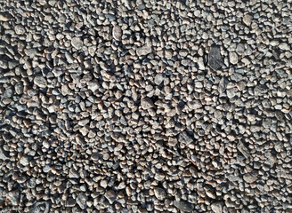 Small granite stones lie on a dirt road, top view in the rays of the midday sun.