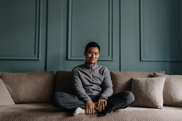 Asian man in fleece sitting in the living room in cold weather.