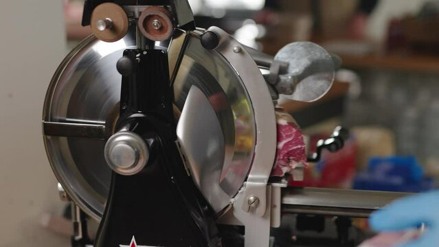 Prosciutto being sliced by hand at an Italian deli. Fresh deli meat being sliced on a meat slicer.