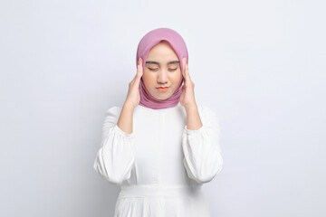 Stressed young Asian Muslim woman touching her temples and having headache isolated over white background