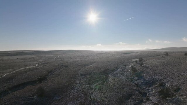 Drone flight over frozen moors and fields lit by a low winter sun in a blue sky.