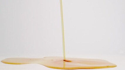 Sticky brown maple syrup pouring into puddle of syrup and splashing on white back drop in slow motion - Powered by Adobe