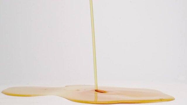 Sticky brown maple syrup pouring into puddle of syrup and splashing on white back drop in slow motion