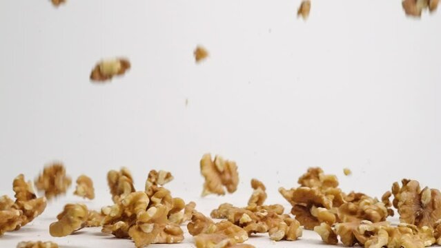 Whole walnut pieces falling onto white table top and bouncing around before landing in a pile in slow motion