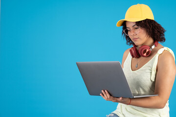 Young woman with glasses and a cap, using a laptop on her hand and headphone