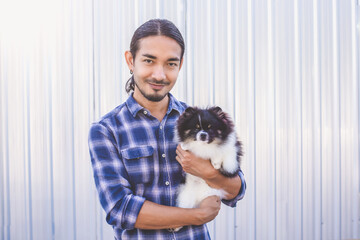 Portrait of a handsome Asian man with long hair wearing a blue checkered shirt and jeans. Hold his Pomeranian and play with it.