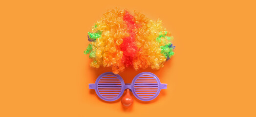 Clown wig and eyeglasses on orange background. April Fools' Day