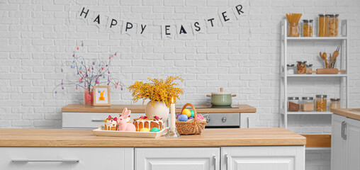 Tray with Easter cakes, mimosa flowers and colorful eggs in basket on counter in kitchen