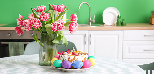 Vase with tulips, Easter cake and colorful eggs on dining table in kitchen