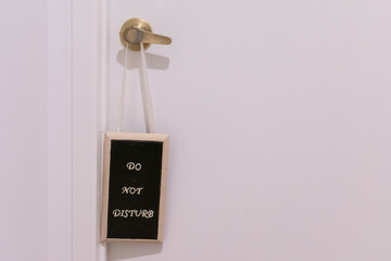 A wooden "do not disturb" sign hanging from a brass door knob