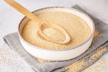 Bowl and spoon of amaranth seeds on light background, closeup