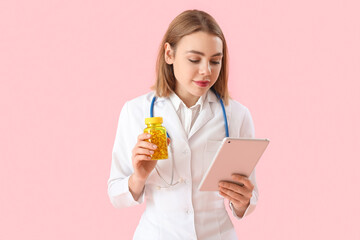 Beautiful doctor with bottle of vitamin supplements and tablet computer on pink background