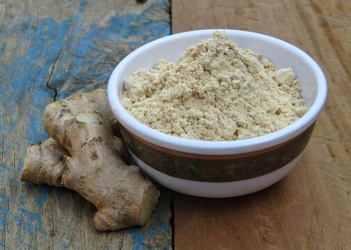 Ginger powder in a bowl on old wooden background 