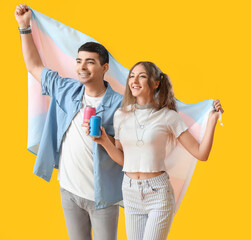 Young couple with transgender flag and soda on yellow background