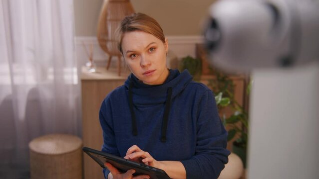 Caucasian woman installs security camera. Woman sets up angle of CCTV camera at home and rotates it with digital tablet computer and application. Tracking system, safety and privacy concept. Zoom out.