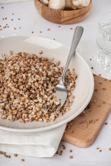 Board with plate of tasty buckwheat porridge on white table